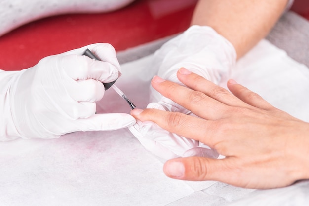 Close-up tiro de uma esteticista aplicando esmalte para unha feminina no salão de beleza.