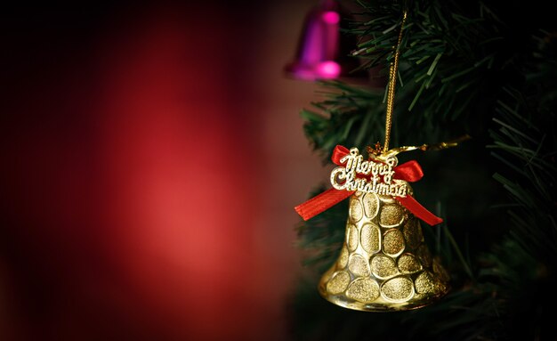 Close-up tiro do sino de brilho dourado brilhante com fita vermelha decoração pendurada no galho de árvore de pinheiro de Natal verde na frente do fundo desfocado na noite de celebração tradicional do festival de véspera de Natal.