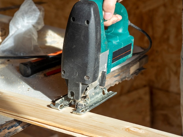 Close-up de un trabajador aserrando una tabla de madera con una sierra de calar eléctrica