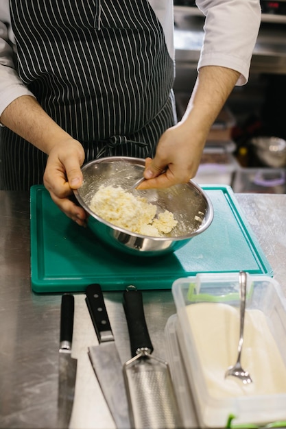 Close-up Um cozinheiro masculino prepara massa de panqueca em uma tigela de metal na cozinha de um restaurante