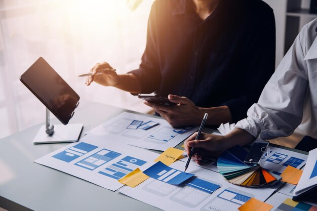 Close up ux desarrollador y ui diseñador lluvia de ideas sobre la interfaz de la aplicación móvil diseño de marco de alambre en la mesa con breif del cliente y código de color en la oficina moderna agencia de desarrollo digital creativa