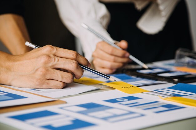 Close up ux desarrollador y ui diseñador lluvia de ideas sobre la interfaz de la aplicación móvil diseño de marco de alambre en la mesa con breif del cliente y código de color en la oficina moderna agencia de desarrollo digital creativa