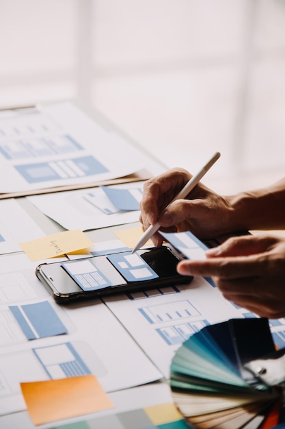 Close up ux desarrollador y ui diseñador lluvia de ideas sobre la interfaz de la aplicación móvil diseño de marco de alambre en la mesa con breif del cliente y código de color en la oficina moderna agencia de desarrollo digital creativa