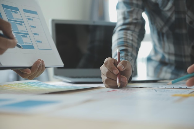 Close up ux desarrollador y ui diseñador lluvia de ideas sobre la interfaz de la aplicación móvil diseño de marco de alambre en la mesa con breif del cliente y código de color en la oficina moderna agencia de desarrollo digital creativa