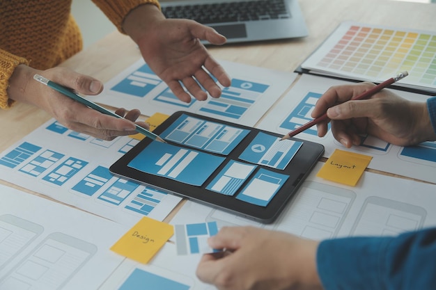 Close up ux desarrollador y ui diseñador lluvia de ideas sobre la interfaz de la aplicación móvil diseño de marco de alambre en la mesa con breif del cliente y código de color en la oficina moderna agencia de desarrollo digital creativa