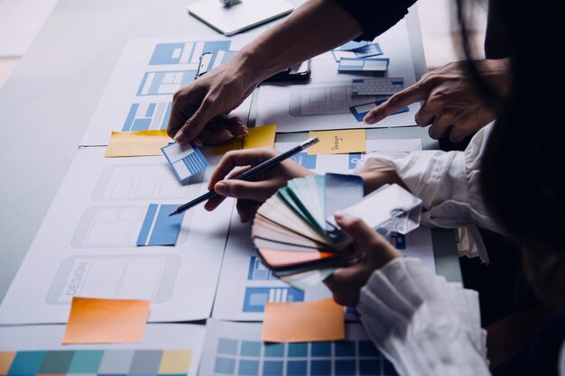 Close up ux desarrollador y ui diseñador lluvia de ideas sobre la interfaz de la aplicación móvil diseño de marco de alambre en la mesa con breif del cliente y código de color en la oficina moderna agencia de desarrollo digital creativa