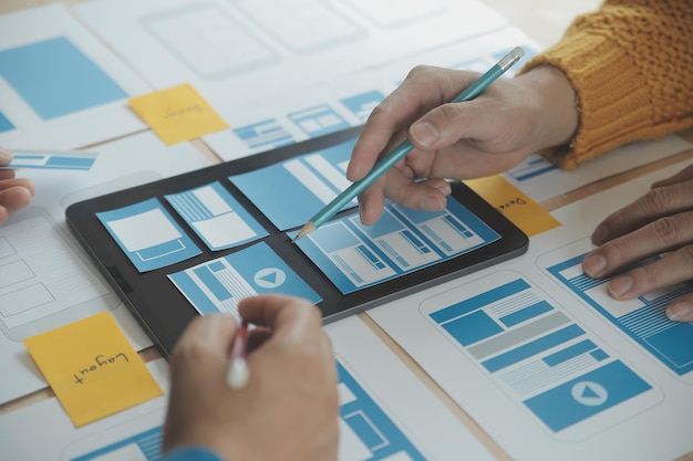 Close up ux desarrollador y ui diseñador lluvia de ideas sobre la interfaz de la aplicación móvil diseño de marco de alambre en la mesa con breif del cliente y código de color en la oficina moderna agencia de desarrollo digital creativa