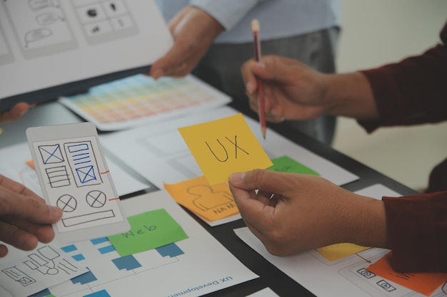 Close up ux desarrollador y ui diseñador lluvia de ideas sobre la interfaz de la aplicación móvil diseño de marco de alambre en la mesa con breif del cliente y código de color en la oficina moderna agencia de desarrollo digital creativa