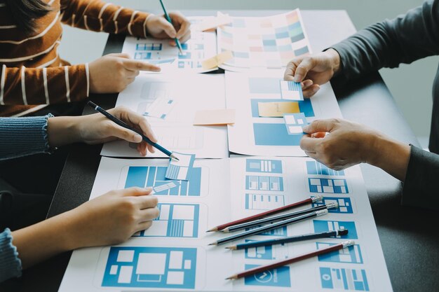 Close up ux desarrollador y ui diseñador lluvia de ideas sobre la interfaz de la aplicación móvil diseño de marco de alambre en la mesa con breif del cliente y código de color en la oficina moderna agencia de desarrollo digital creativa
