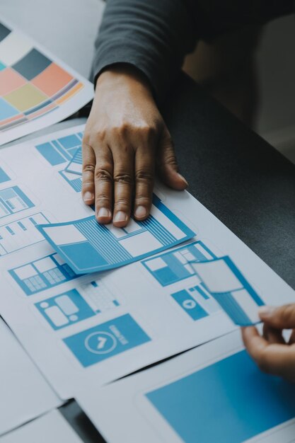 Close up ux desarrollador y ui diseñador lluvia de ideas sobre la interfaz de la aplicación móvil diseño de marco de alambre en la mesa con breif del cliente y código de color en la oficina moderna agencia de desarrollo digital creativa