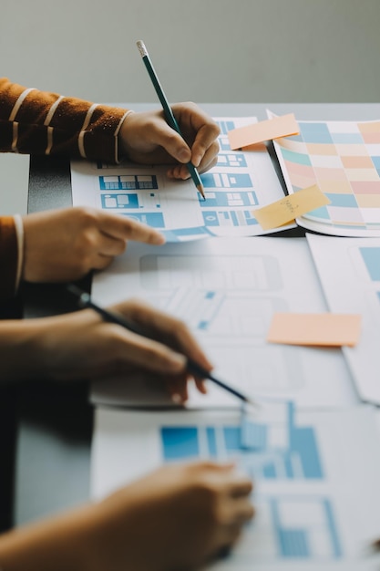Close up ux desarrollador y ui diseñador lluvia de ideas sobre la interfaz de la aplicación móvil diseño de marco de alambre en la mesa con breif del cliente y código de color en la oficina moderna agencia de desarrollo digital creativa