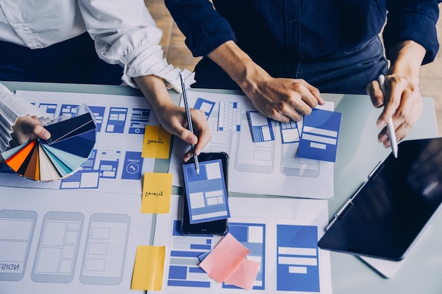 Close up ux desarrollador y ui diseñador lluvia de ideas sobre la interfaz de la aplicación móvil diseño de marco de alambre en la mesa con breif del cliente y código de color en la oficina moderna agencia de desarrollo digital creativa