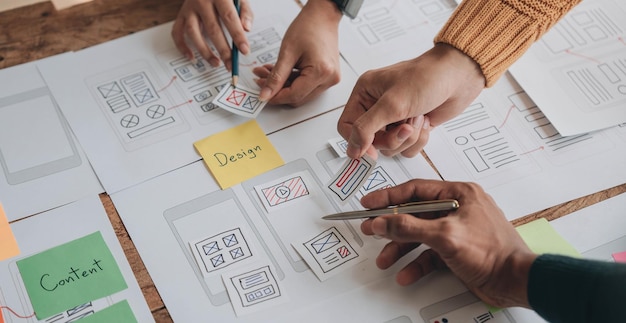 Close up ux desarrollador y ui diseñador lluvia de ideas sobre la interfaz de la aplicación móvil diseño de marco de alambre en la mesa con breif del cliente y código de color en la oficina moderna agencia de desarrollo digital creativa