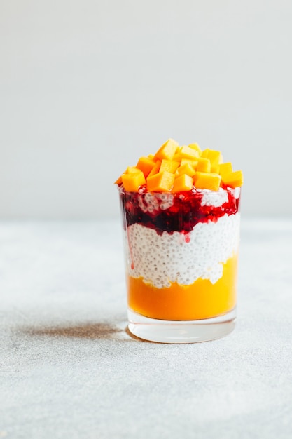 Close-up de un vaso de pudín de chía con yogur de calabaza y mermelada sobre un fondo gris