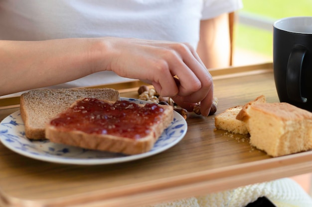 Close-up vista da mão de uma mulher colhendo nozes secas de uma bandeja de café da manhã com torradas de morango, café e bolo