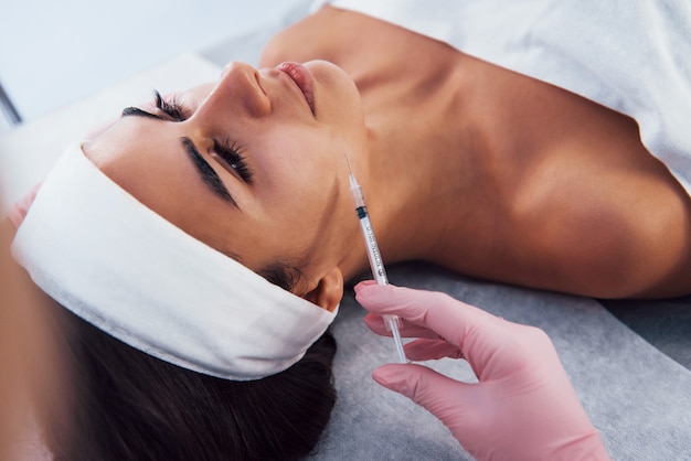 Close-up vista da mulher deitada no salão spa e tenha a injeção pela seringa na pele do rosto.