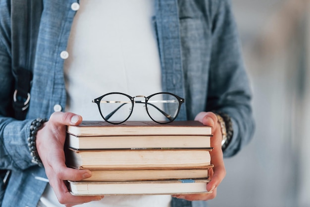 Close-up vista de ale jovem estudante em roupas jeans que está no corredor de uma faculdade com livros com óculos nas mãos
