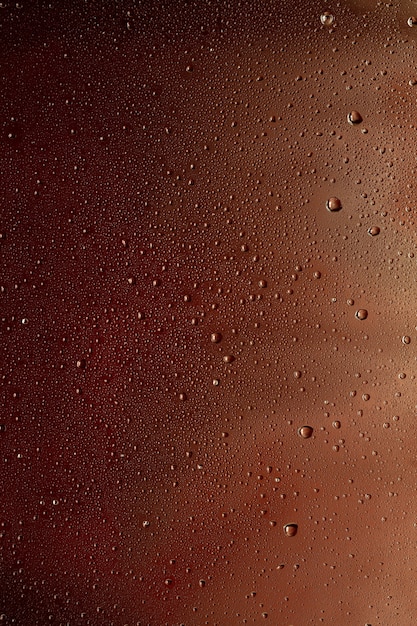 Close-up vista de gotas de frio no copo de fundo de cerveja. Textura de refrigerante de bebida alcoólica com macro bolhas na parede de vidro. Fizzing ou flutuando até o topo da superfície. De cor castanha escura.