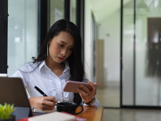 Close-up vista de mulher freelancer procurando informações no smartphone e anote na sala de escritório