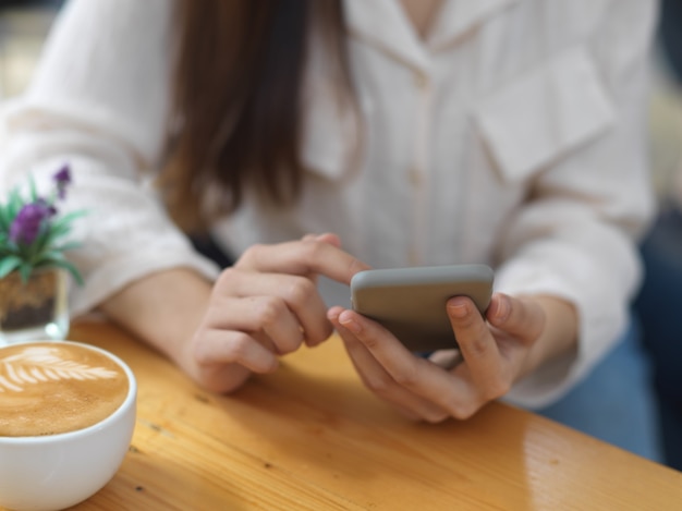 Close-up vista de mulher usando smartphone enquanto relaxa sentado com uma xícara de café no café