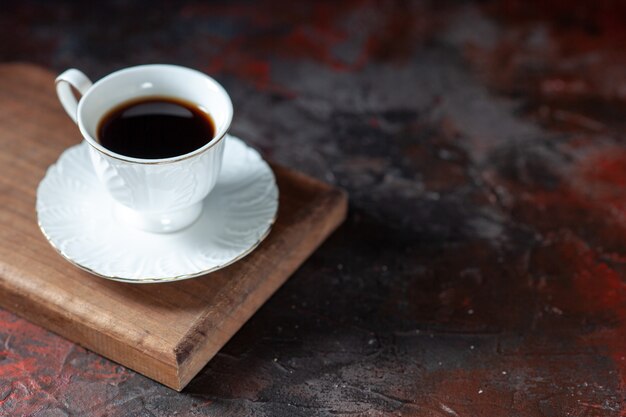 Close-up vista de um delicioso café em uma xícara branca em uma placa de madeira marrom no fundo escuro de mistura de cores com espaço livre