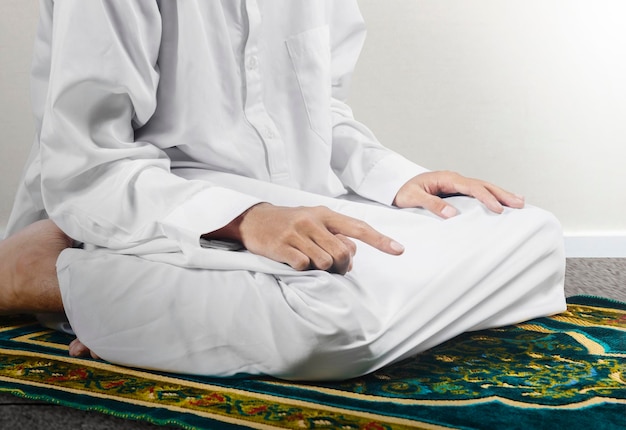 Close-up vista de um homem muçulmano em uma posição de oração salat em um tapete de oração com fundo de parede branca