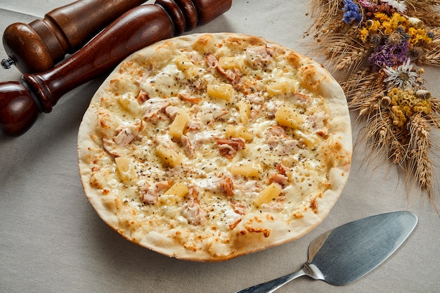 Close-up vista na apetitosa pizza havaiana com queijo derretido, bacon, frango e abacaxi numa toalha de mesa cinza de linho em um restaurante. Pizza em composição. Cozinha italiana. Lay plana de alimentos