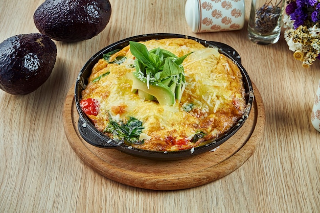 Close-up vista na omelete de Frittata espanhola caseiro com tomate espinafre, abacate e cereja em uma panela preta sobre uma mesa de madeira. Cozinha espanhola. Almoço saboroso