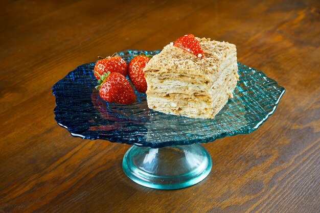 Close-up vista no pedaço de bolo Napoleão com morango na chapa azul na mesa de madeira. Cozinha russa, bolo em várias camadas com creme de confeiteiro