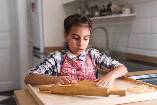 Foto close-up vista sobre a linda garotinha rolando massa na cozinha. mãos de menina rolando massa na mesa da cozinha. mãos de criança cozinhando com rolo.