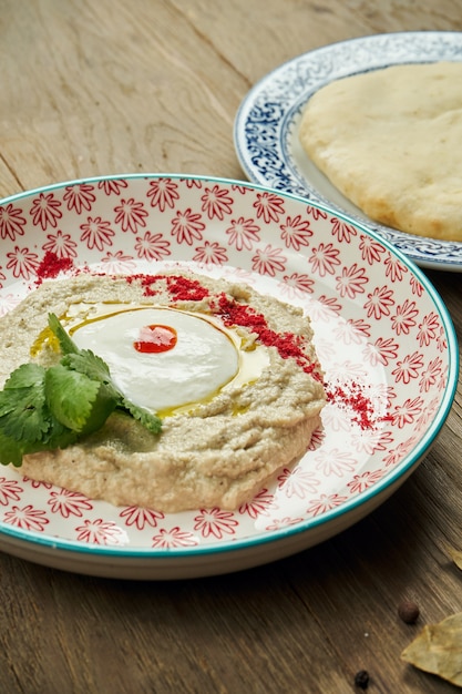 Close-up vista sobre Baba ghanoush - aperitivo de Levantine de purê de berinjela cozida misturada com tahine com molho de iogurte em um prato de cerâmico em uma superfície de madeira