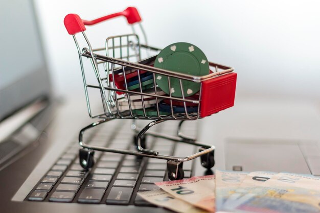 Foto close-up von einkaufswagen mit glücksspiel-chips durch papierwährung auf laptop