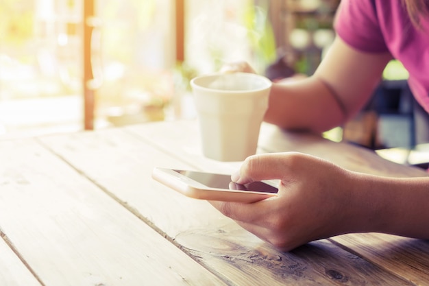 Close up von schönen jungen Hipster Frau Hände halten mobile Smartphone mit heißen Kaffeetasse im Café-Shop, weiblich mit Handy. Vintager Farbton