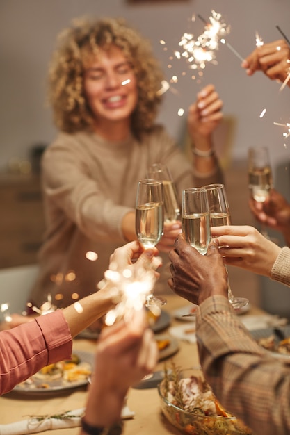 Close vertical de pessoas brindando com taças de champanhe enquanto desfrutam de um jantar com amigos e familiares segurando estrelinhas