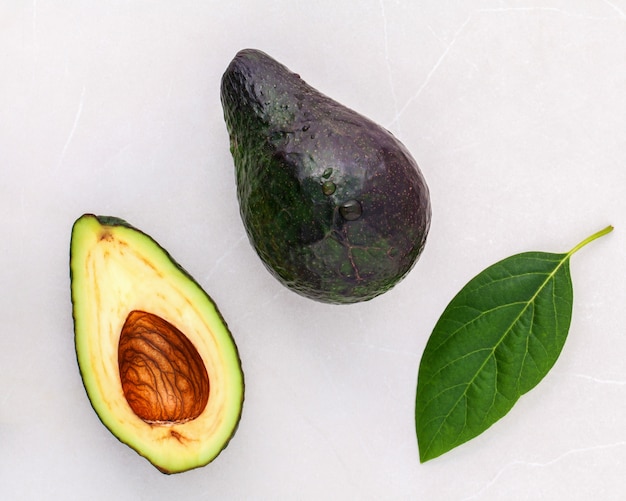 Closeup aguacate fresco y hojas sobre fondo de mármol.