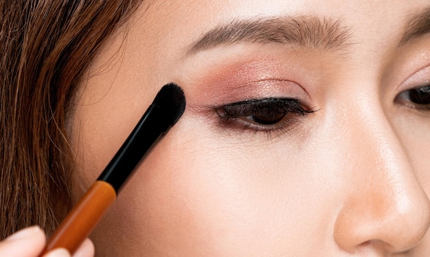 Closeup ardiente mujer joven con piel sana y clara aplicando su sombra de ojos con pincel Modelo femenino con maquillaje de moda Concepto de belleza y maquillaje