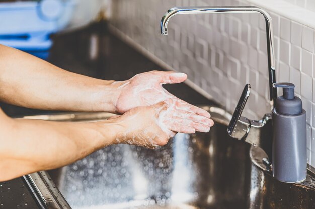 Closeup asiático lavando as mãos com água da torneira na cozinha de casa