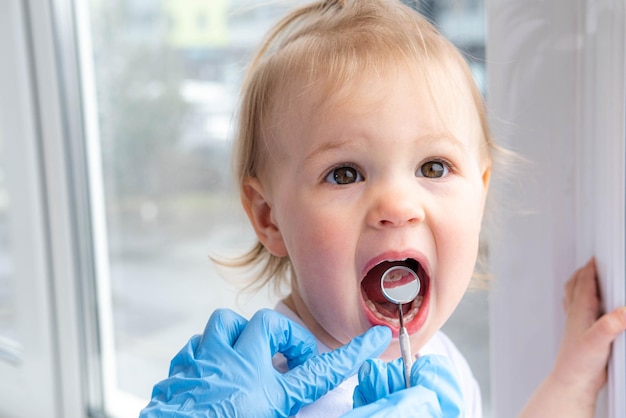 Closeup boca aberta criança e espelho nas mãos dos dentistas no exame de luvas azuis examinam o tratamento dos dentes para cuidados de saúde infantil higiene dental das crianças