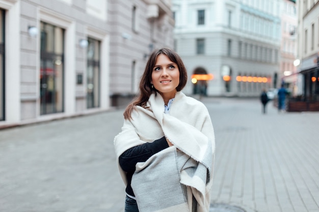 Closeup calle elegante retrato de mujer morena joven sonriendo y divirtiéndose en el frío bajo una gran bufanda de lana