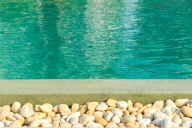 Closeup da fronteira de pedra na frente da piscina azul brilhante. Decoração e design de piscinas com reflexo da luz solar, férias, relax, conceito de fuga