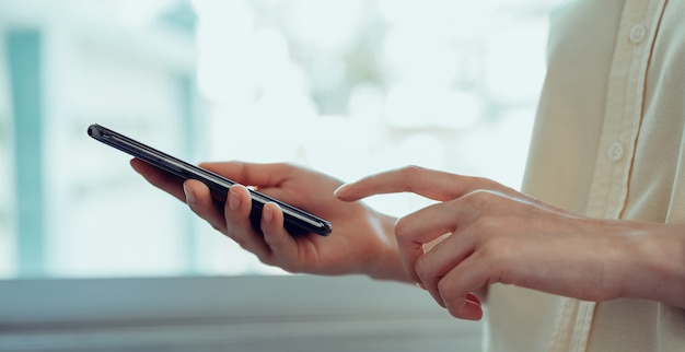 Closeup da mão da jovem mulher segurando o smartphone e conversando com os amigos na rede social.