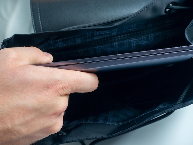 Closeup da mão de uma mulher colocando um laptop cinza em uma bolsa preta o conceito de trabalhar em casa trabalho remoto freelance Foco seletivo