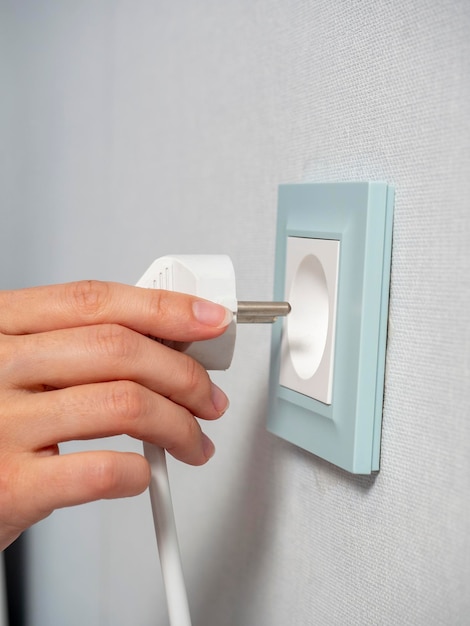 Closeup da mão de uma mulher segurando um plugue branco e prestes a conectá-lo a uma tomada azul na parede da casa o conceito de conservação de energia foco seletivo de vista lateral