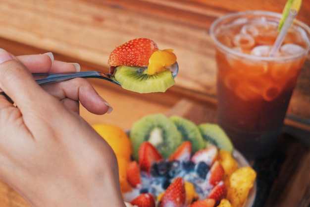 Closeup da mão de uma mulher segurando uma colher de salada de frutas