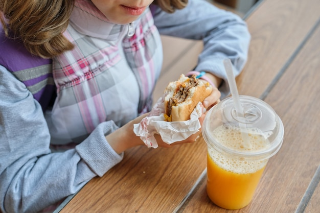 Closeup da mão do garoto comendo hambúrguer e bebendo suco de laranja