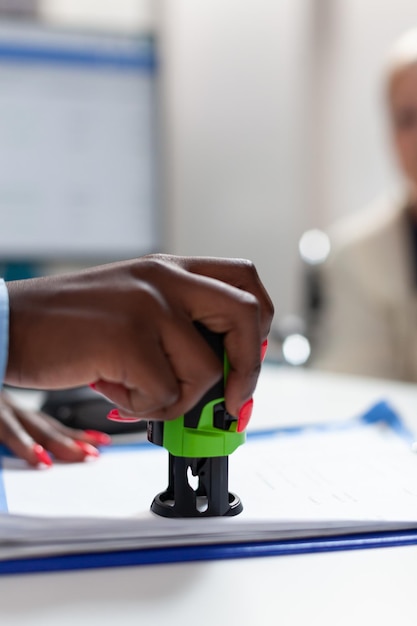 Foto closeup da mão do médico terapeuta americano africano carimbando o papel com prescrição de medicamentos no escritório do hospital. médico médico explicando os resultados do teste para a mulher sênior durante a consulta médica