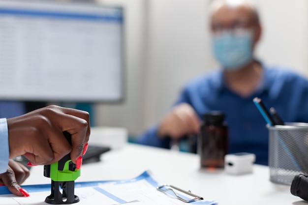 Foto closeup da mão do médico terapeuta carimbando a prescrição de medicamentos discutindo o tratamento de saúde com o homem doente com deficiência durante a consulta clínica no escritório do hospital. conceito de coronavírus