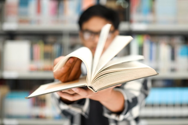 Closeup da mão lançando o livro contra o fundo desfocado das estantes