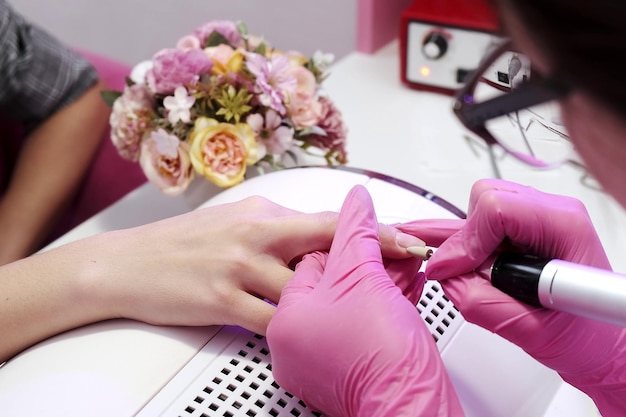 Closeup da menina fazendo uma manicure em um salão de beleza Cuidados com as unhas Manicure em luvas cor de rosa lustra uma unha com um afresco para aplicar verniz Manicure de hardware revelada Procedimento cosmético