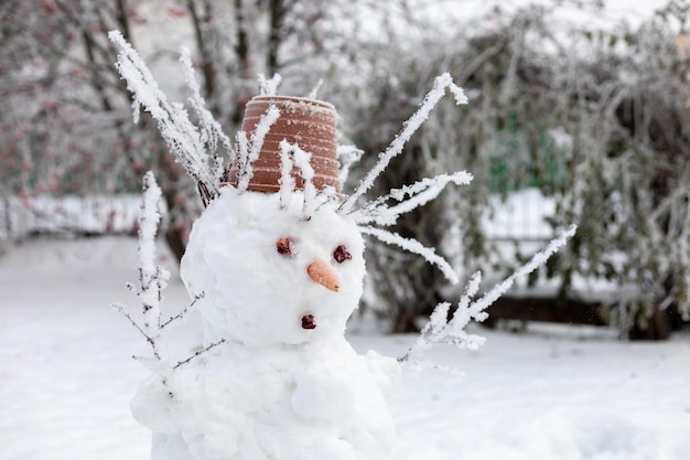 Closeup da parte superior do homem de neve feito por adultos com galhos de árvore de nariz de cenoura em vez de mãos e olhos de cone de cabelo e vaso de flores na cabeça passando tempo de inverno nevado juntos como família